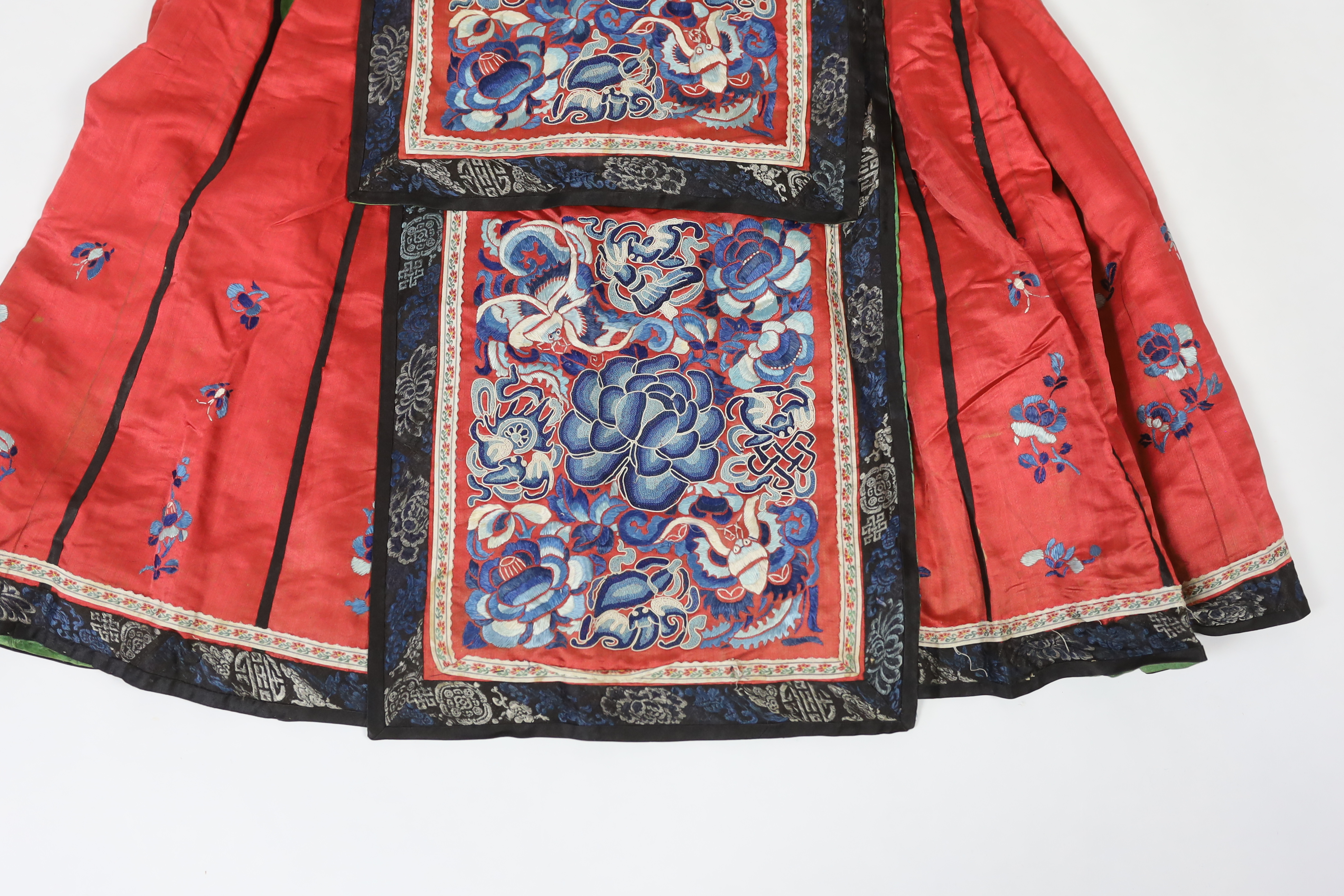 A Chinese red silk skirt, embroidered with a blue silk panel of Chinese knotting flowers and auspicious symbols, the bottom of the skirt with spot motifs bordered with embroidered braiding and ribbon, the slant is lined